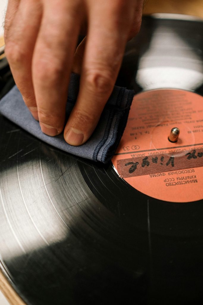 A hand gently wipes a vintage vinyl record on a turntable with a soft cloth, preserving its analog charm.